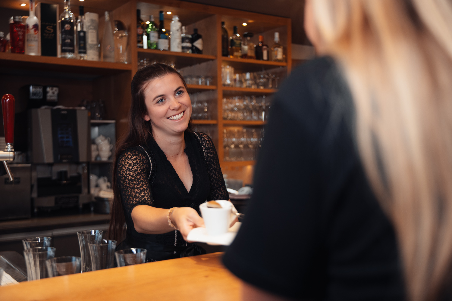 Servicemitarbeiterin reicht einem Gast eine Tasse Kaffee.