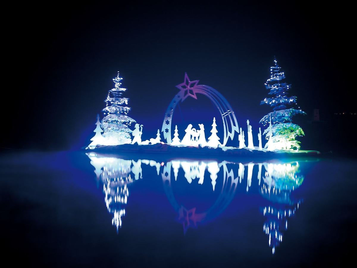 © Kärnten Werbung, Franz Gerdl Beleuchtete Weihnachtskrippe mit Tannenbäumen spiegelt sich nachts im Wörthersee..