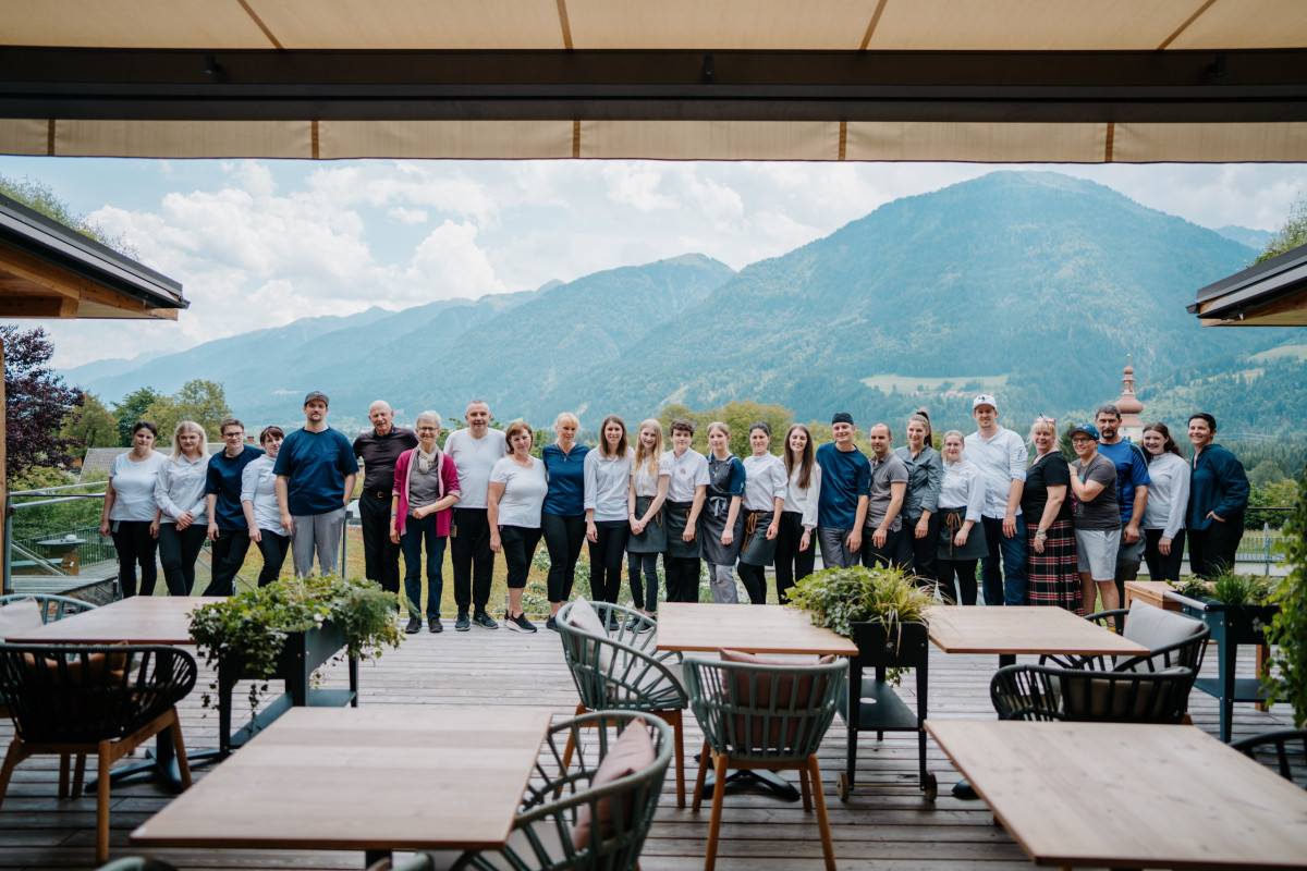 Team des Biohotels Daberer steht gemeinsam auf einer Terrasse mit Blick auf grüne Berge und alpines Tal.