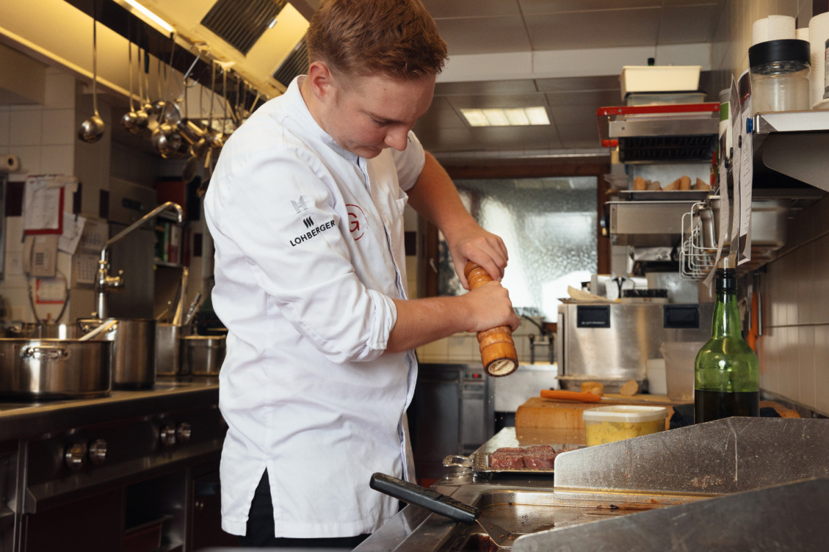 A chef seasons a piece of meat in the kitchen.