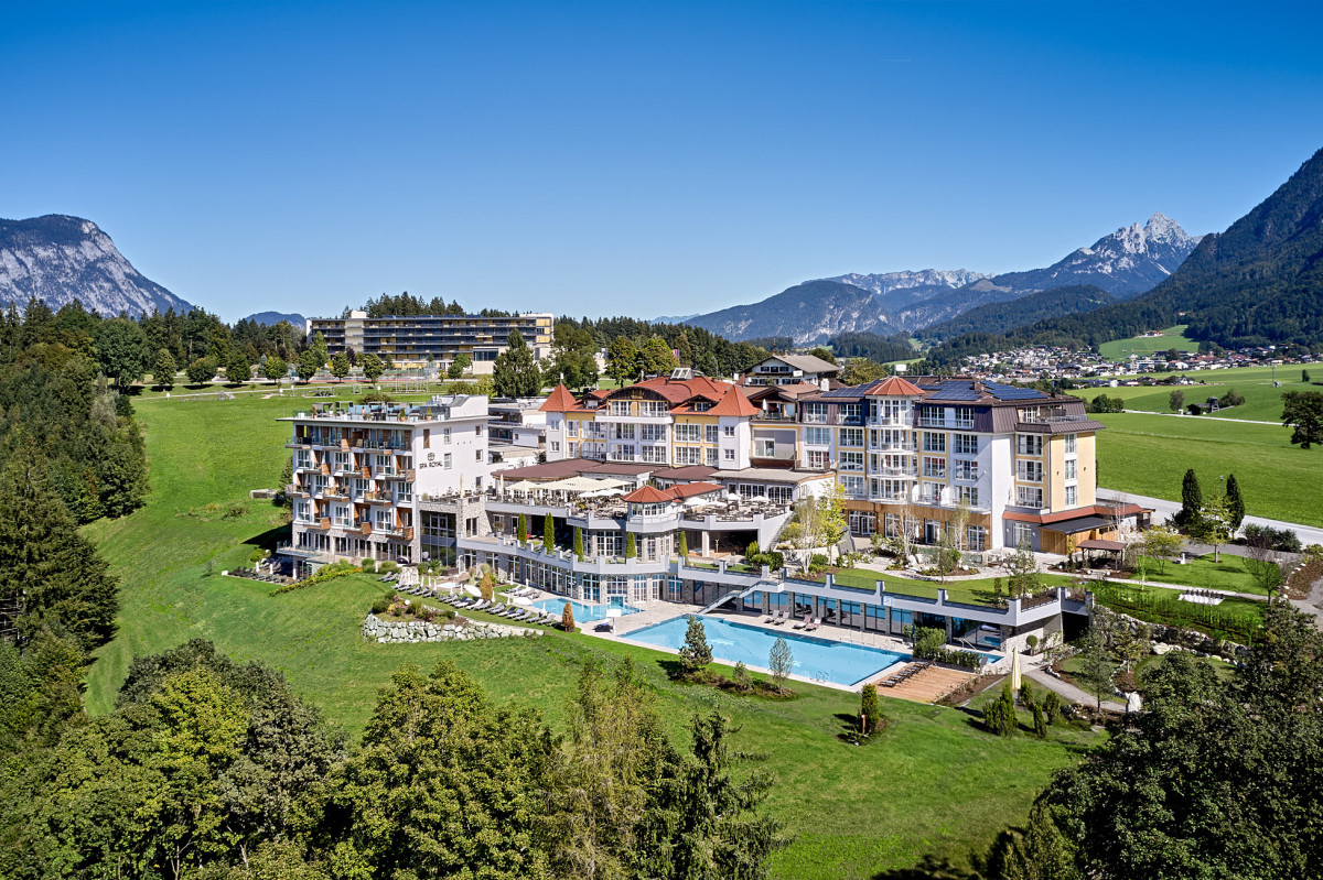 Hotel Panorama Royal im Sommer mit Bergen im Hintergrund und einem Pool vor dem Hotelgebäude.