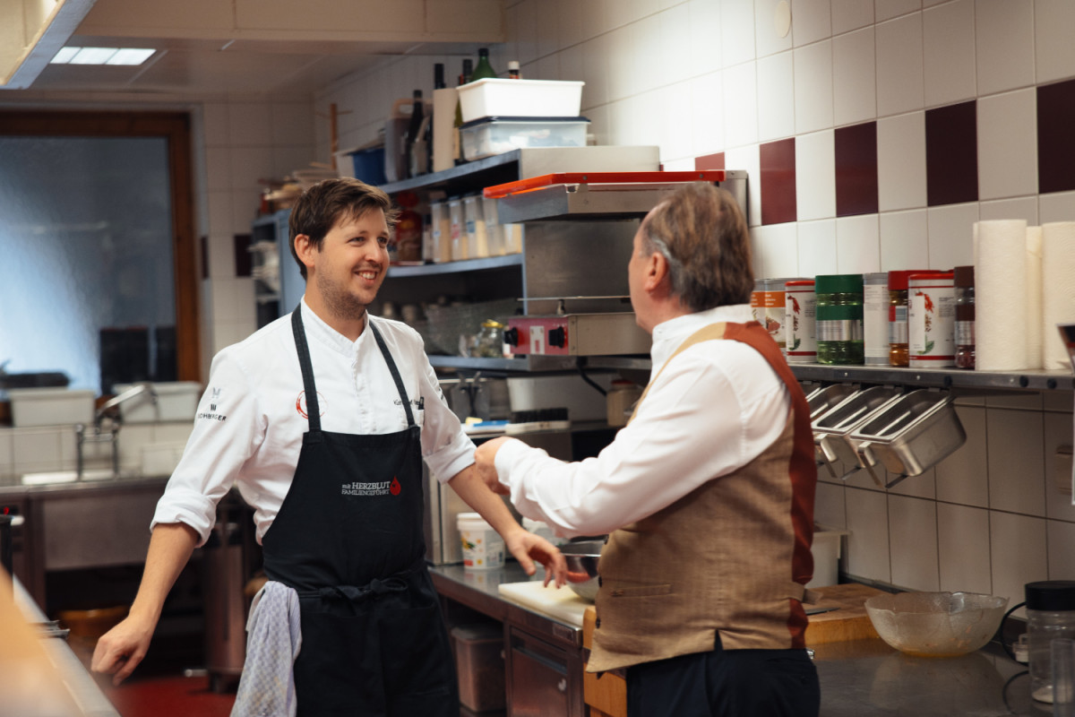 Ein Kellner und ein Koch stehen in der Küche und sprechen miteinander.