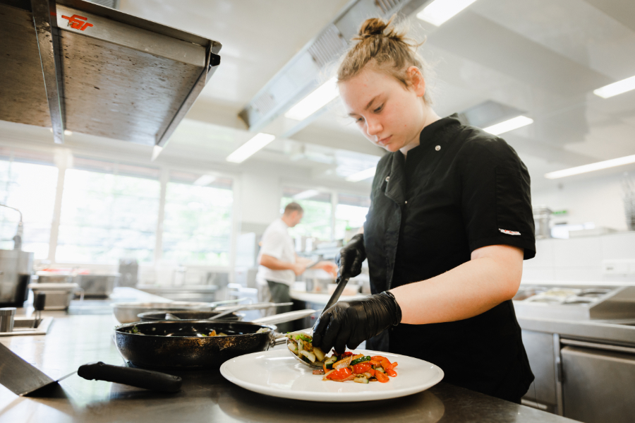 Mitarbeiterin in der Küche richtet ein Gericht professionell an