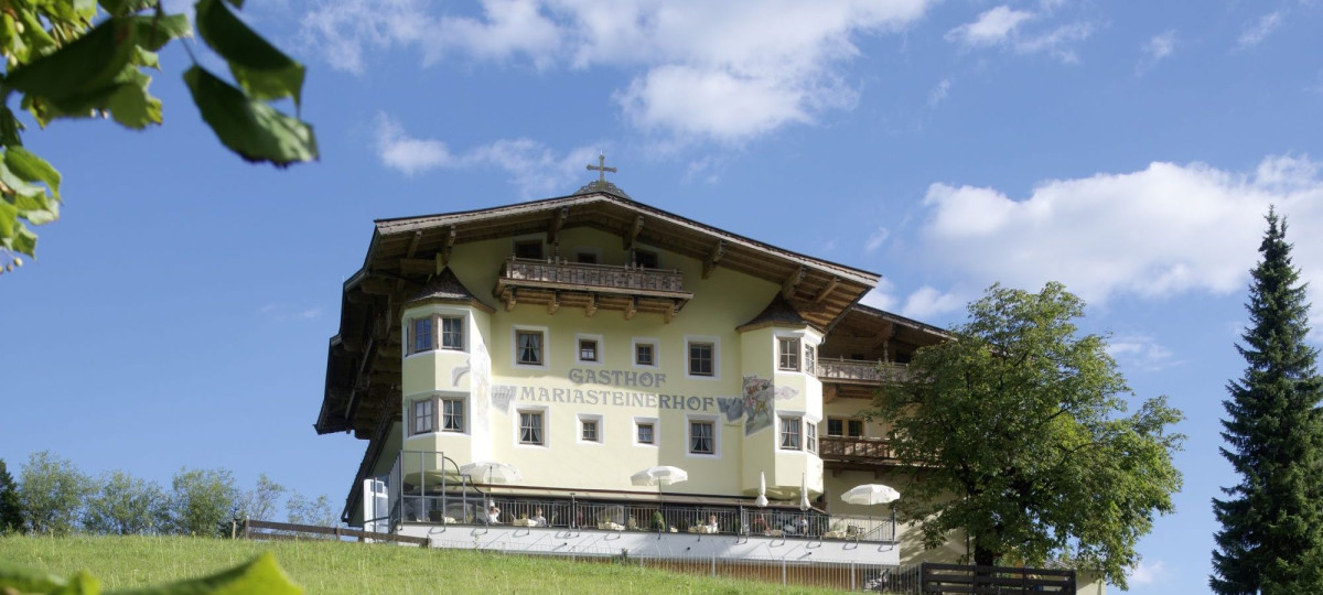 Gasthof Mariasteinerhof im Sommer auf einem Grashügel mit Bäumen.