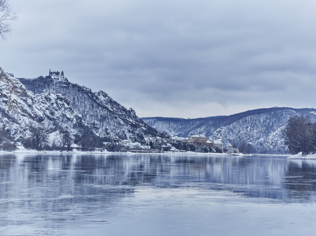 Winterlicher Blick auf die Donau bei Dürnstein in der Wachau mit verschneiten Hängen und Burgruine.