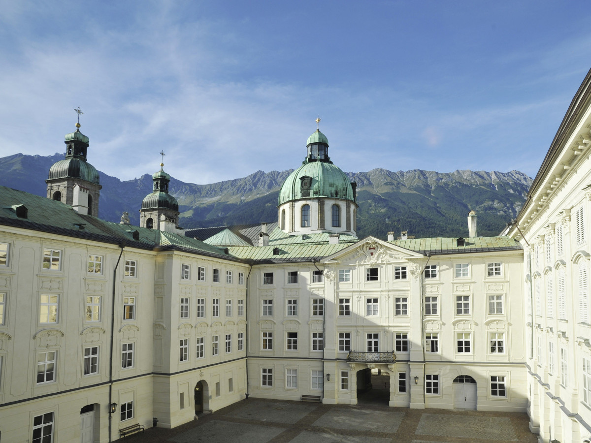 © Tirol Werbung, Bernhard Aichner Die Hofburg in Innsbruck mit leeren Innenhof und Alpenlandschaft im Hintergrund.