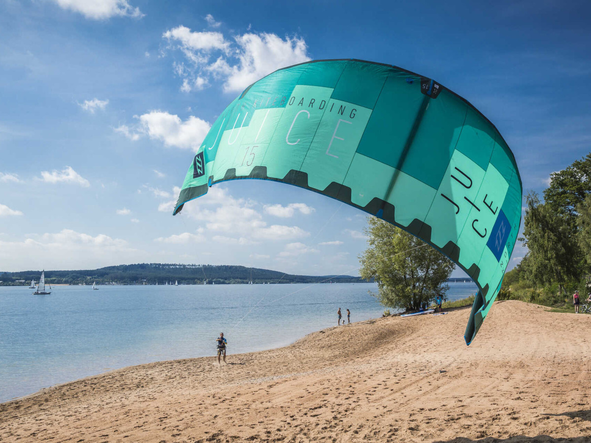 © erlebe.bayern, Bernhard Huber Kitesurf-Schirm am Strand des Brombachsees mit Segelbooten auf dem Wasser im Hintergrund.