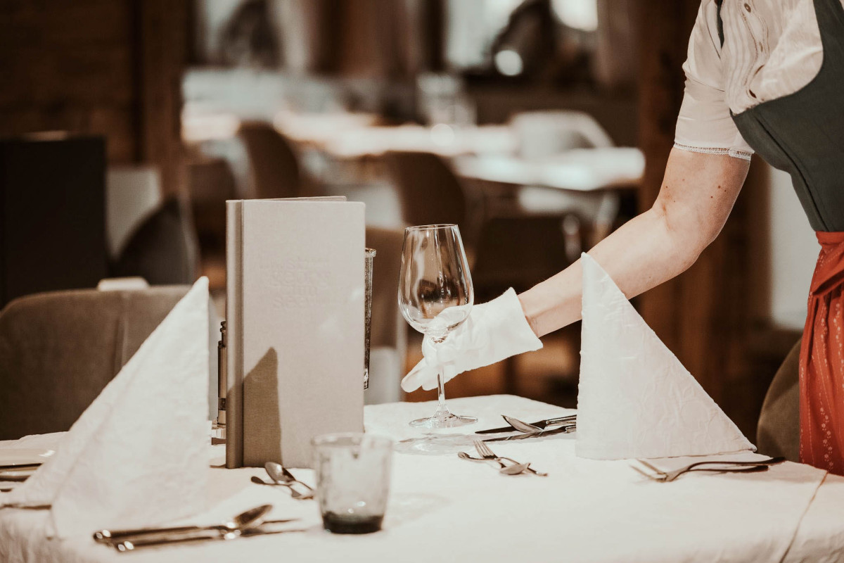 Image Two Servicekraft richtet ein Weinglas auf einem gedeckten Tisch in einem Restaurant aus.