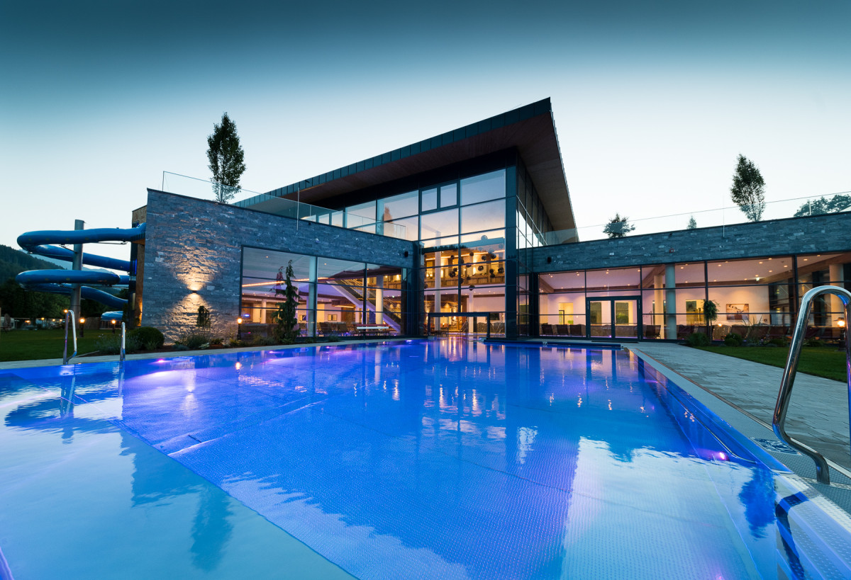 Aussenansicht inklusive beleuchteten Pool des Sportcamps Woferlgut bei Abenddämmerung.