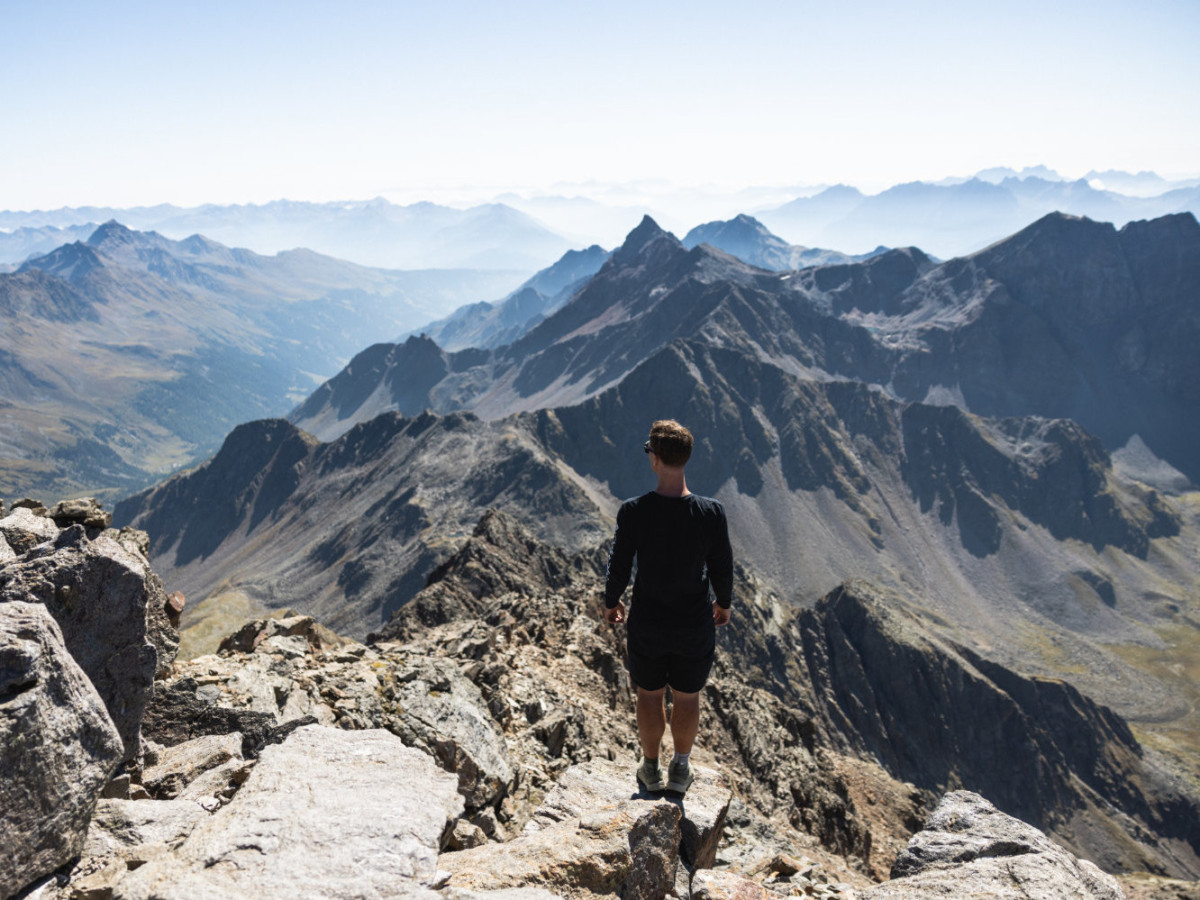 © Satellite Creative House Junger Wanderer blickt vom Gipfel auf, auf die Tiroler Bergwelt.