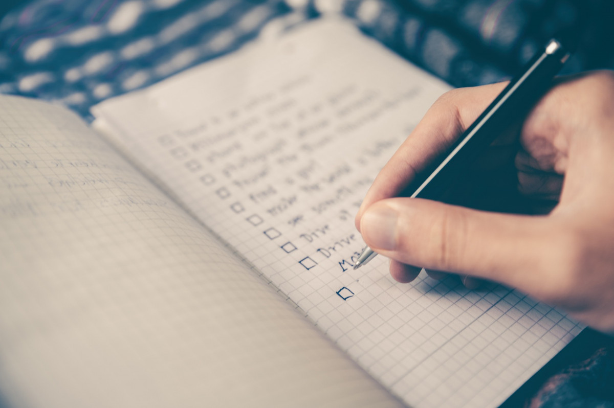 Someone writing a checklist in a notebook.