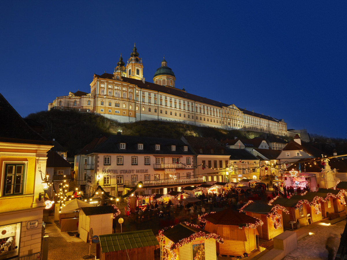 Beleuchteter Adventmarkt vor dem Stift Melk bei Abenddämmerung.