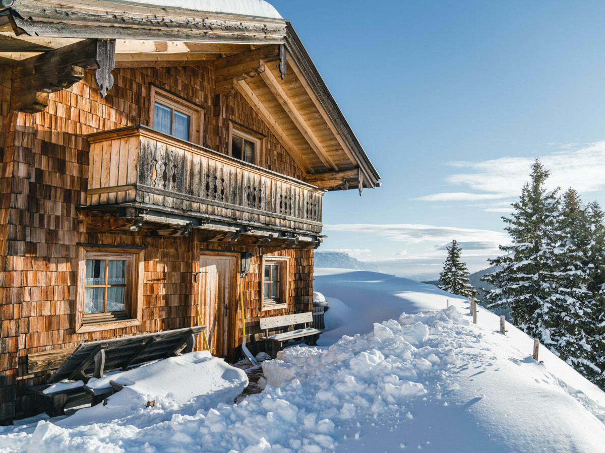 © SalzburgerLand Tourismus Verschneite Berghütte aus Holz mit Balkon und Blick auf die winterliche Alpenlandschaft im Bundesland Salzburg.