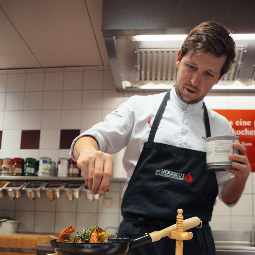 Koch würzt ein Gericht in der Restaurantküche