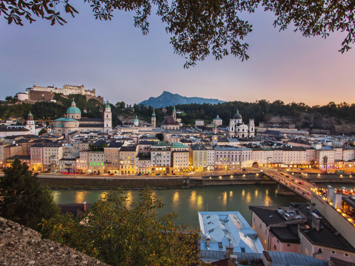 © SalzburgerLand Tourismus Blick auf die Salzburger Altstadt mit Festung Hohensalzburg, Salzach und beleuchteten Häusern in der Dämmerung.