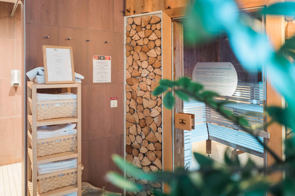 Image Three Saunabereich mit Handtüchern, gestapeltem Holz und geöffneter Glastür zur Holzsauna.