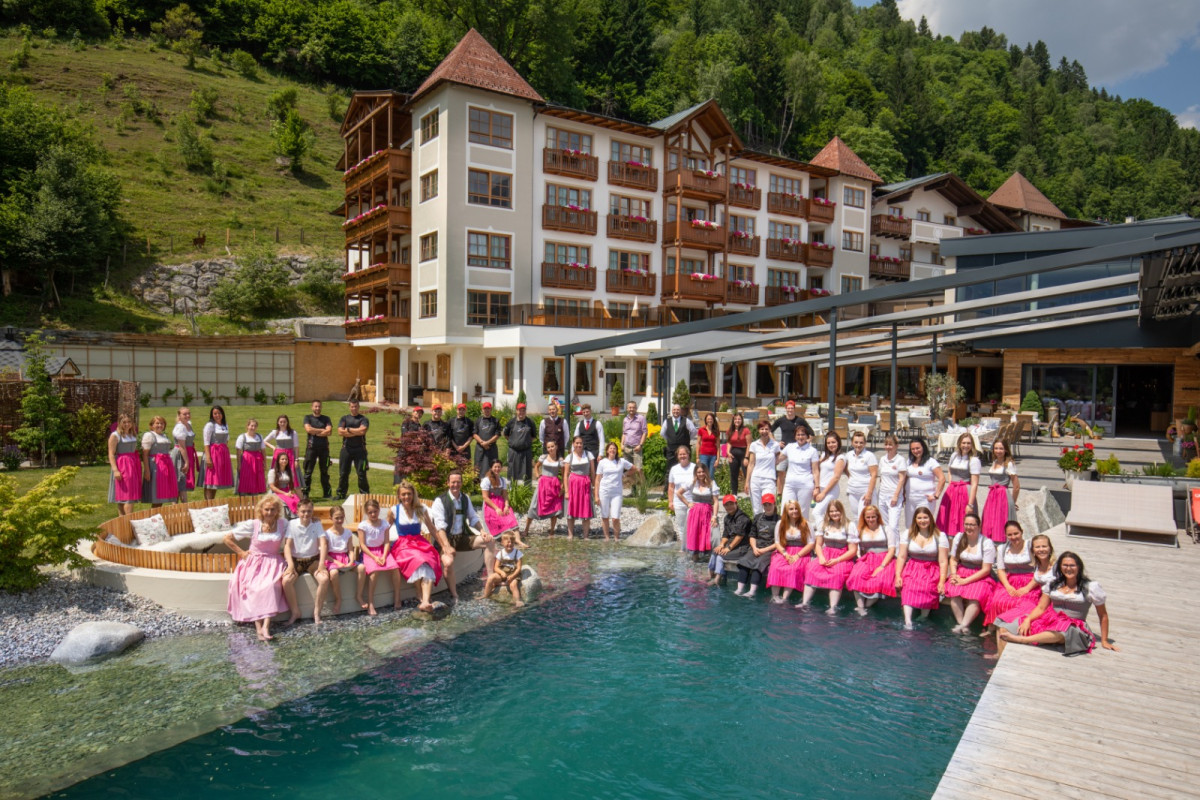 Hotel Alpenblick The team of Hotel Alpenblick in traditional attire by the pool, with the hotel in the background.