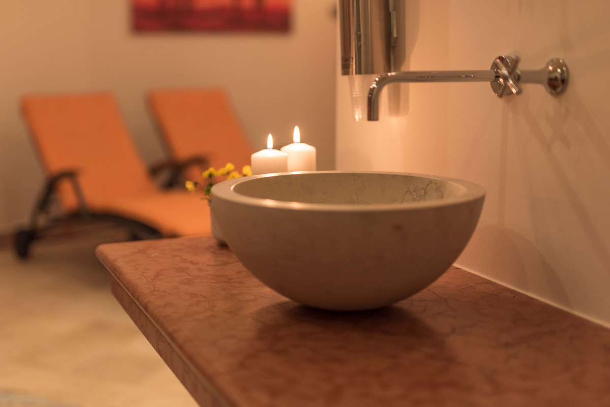 Image One Steinwaschbecken mit Kerzen und Liegen in einem warm beleuchteten Wellnessbereich.