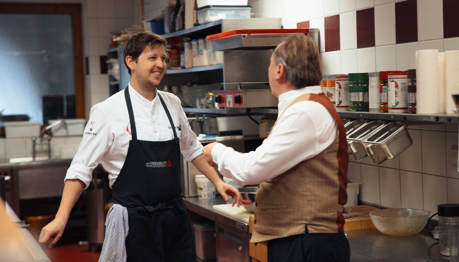 A chef talks to a service staff member in the kitchen.